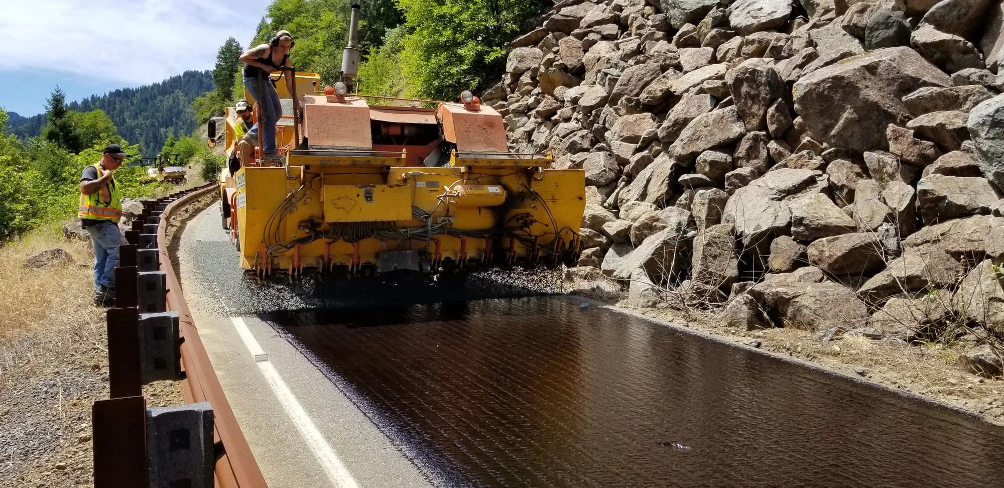 Road crew operating an asphalt paving machine on a rural road.