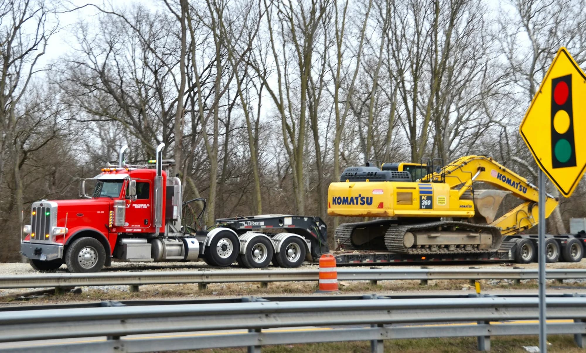 Red Peterbilt tractor hauling a Komatsu excavator on a drop-deck lowboy trailer.