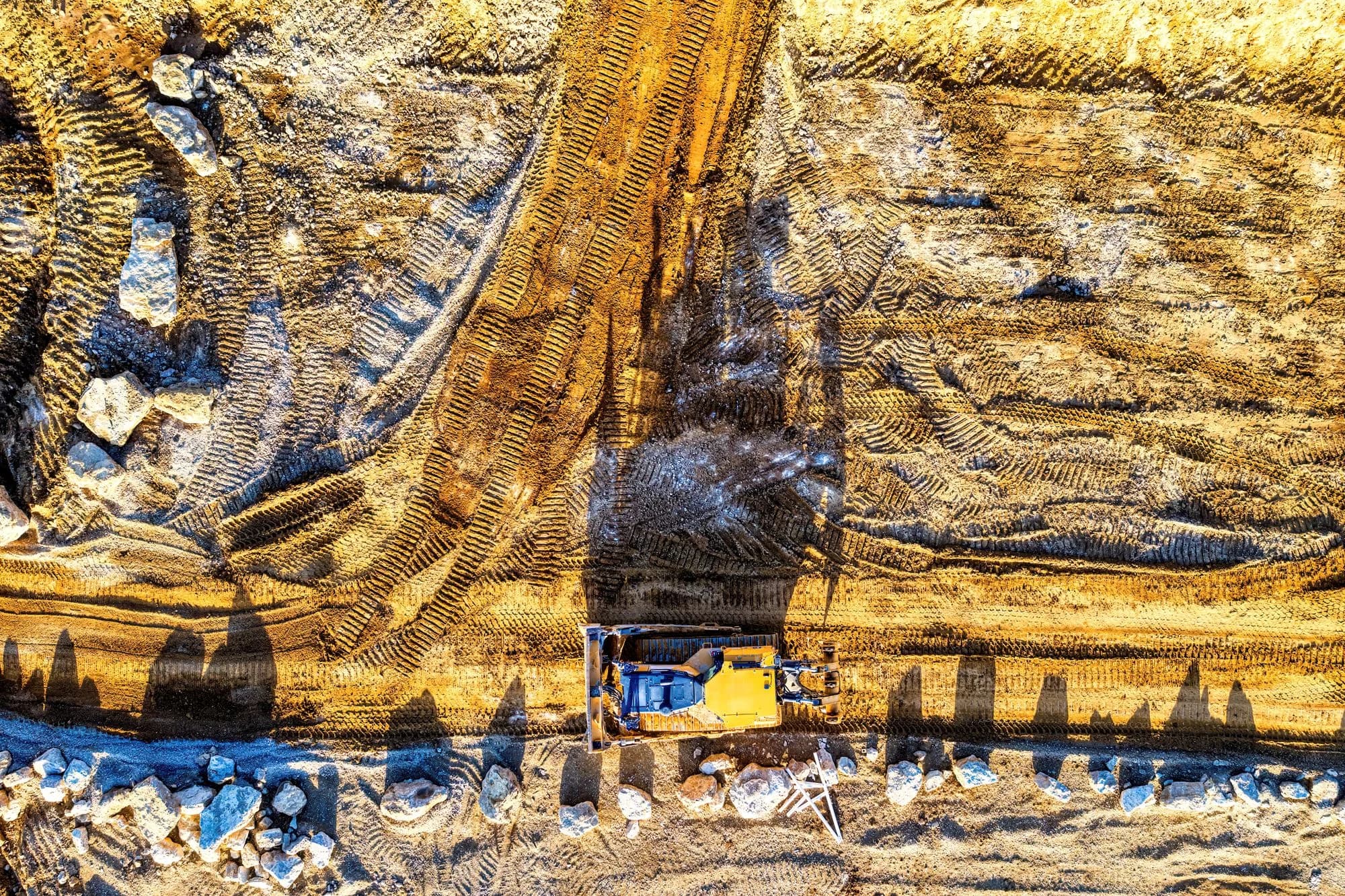 Aerial view of an excavator on an earthwork site with exposed soil and track marks.