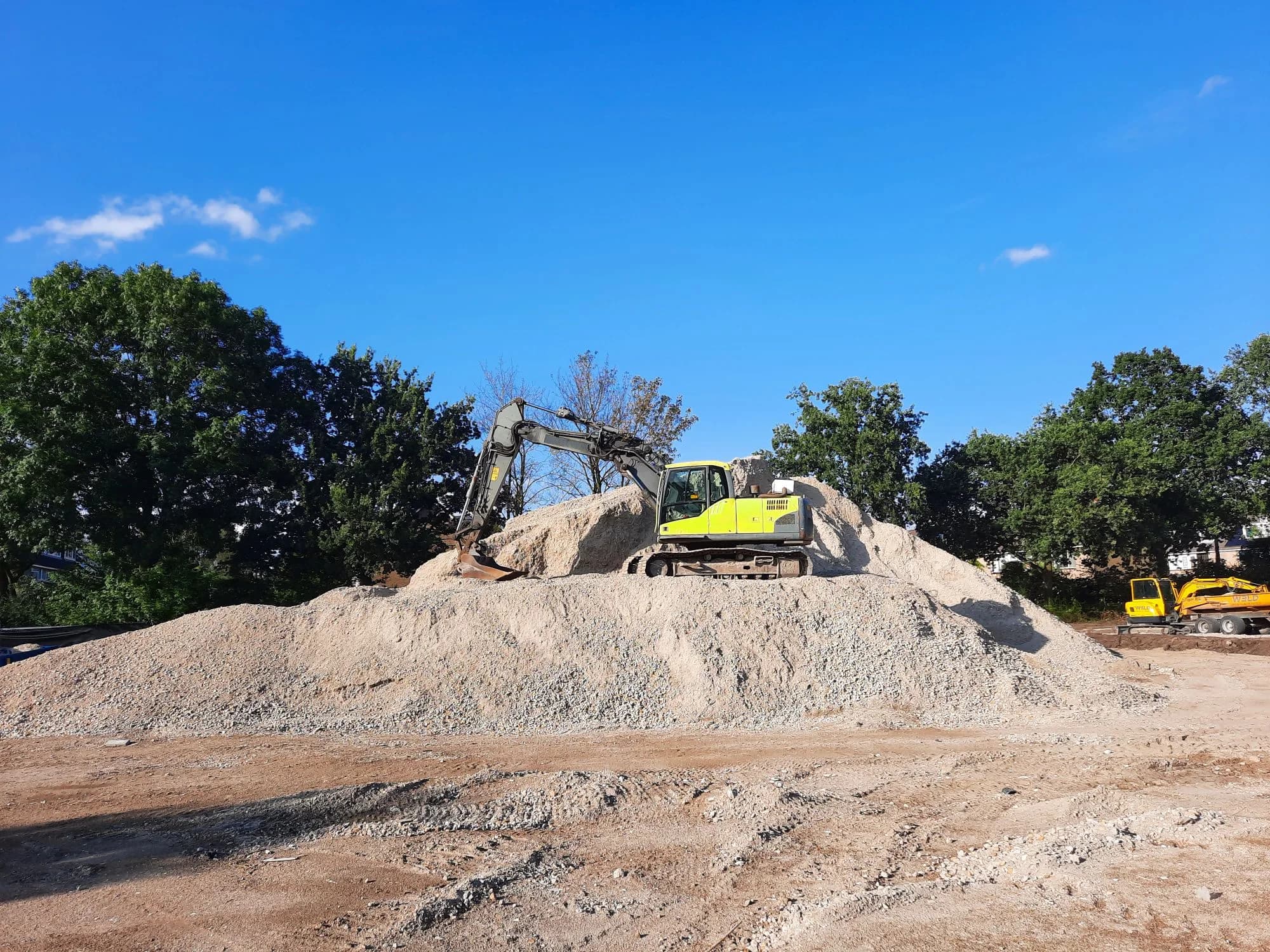 Excavator working on a gravel mound beneath a blue sky.