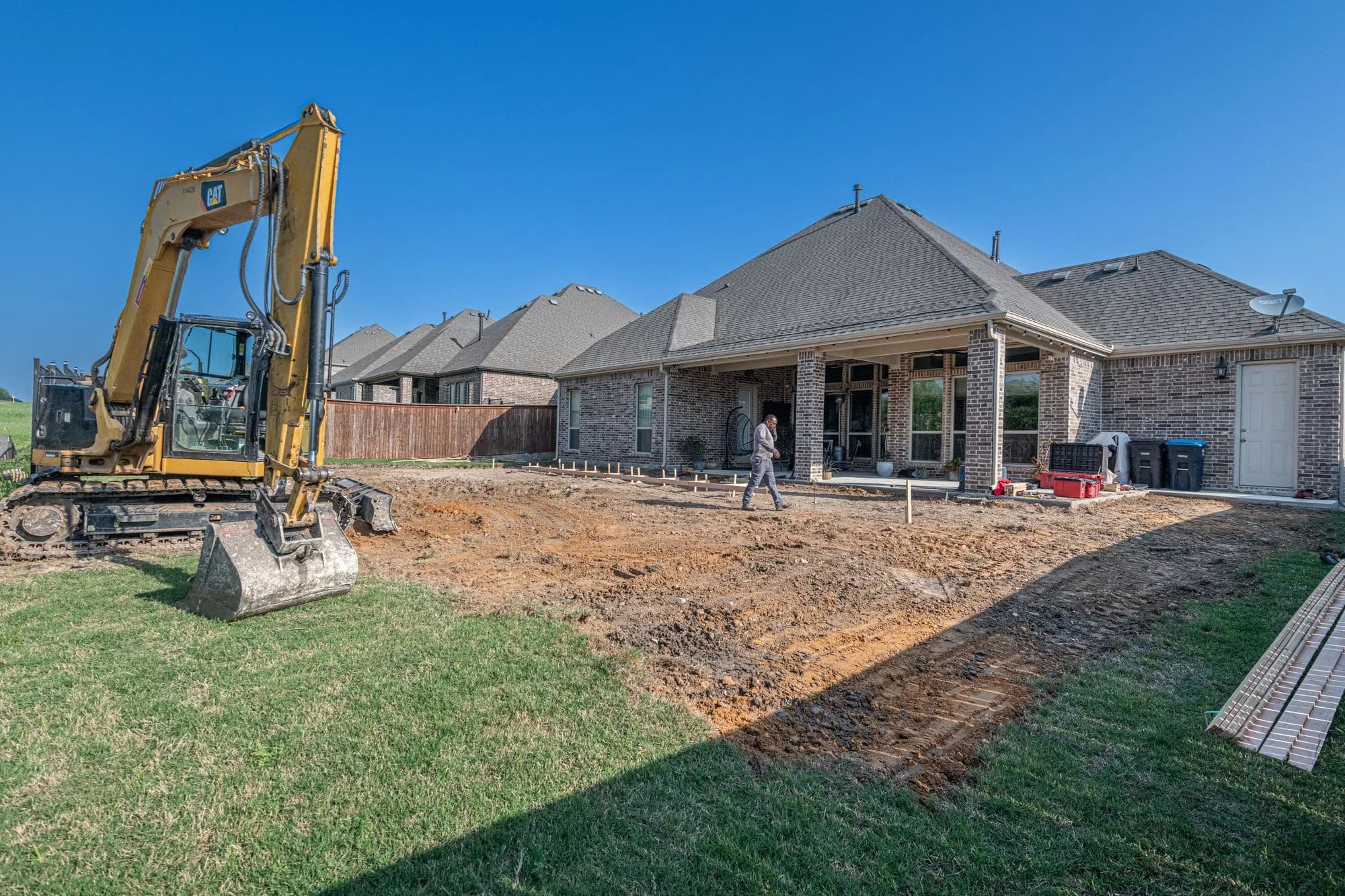 Backyard patio construction with earthmoving machinery beside a home.