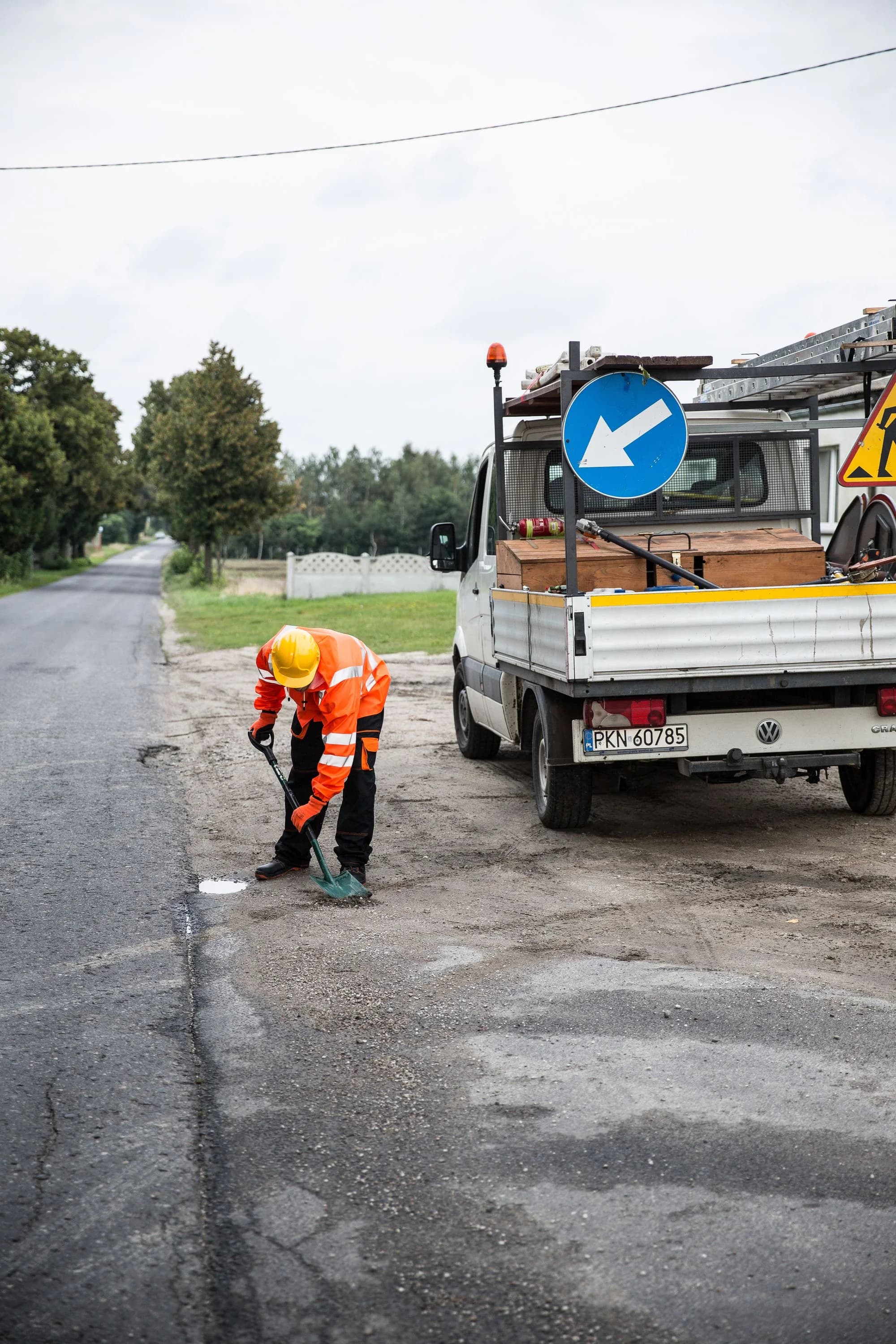 Road maintenance worker repairing a pothole beside a truck.