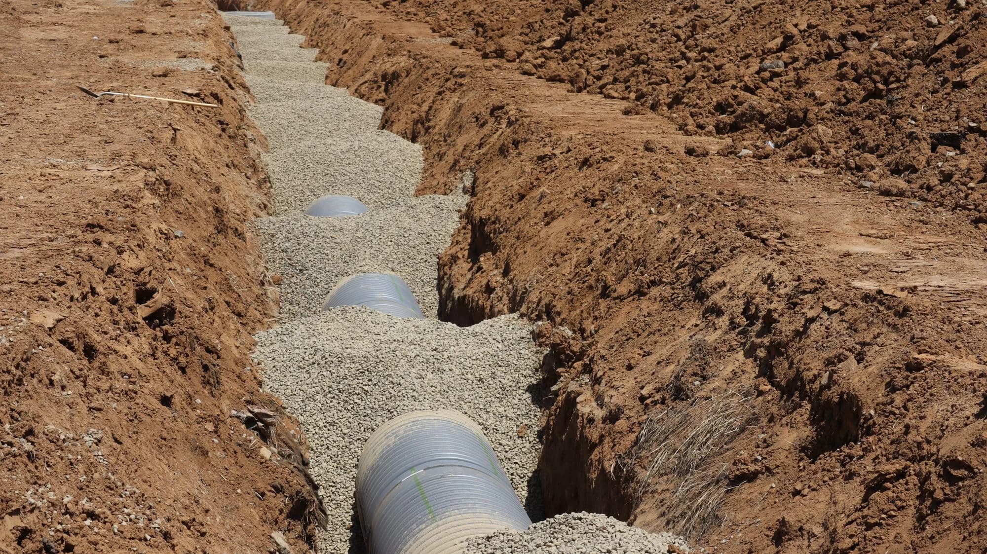 Drainage pipe laid inside an excavated utility trench.